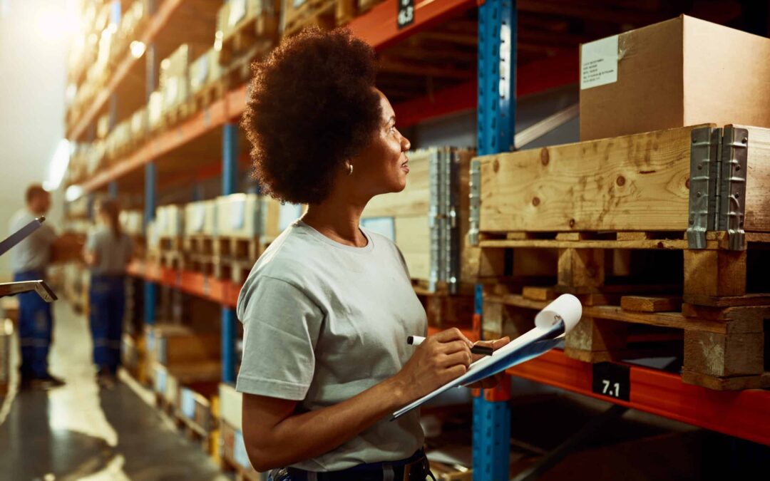 Black female warehouse worker taking notes while checking stock