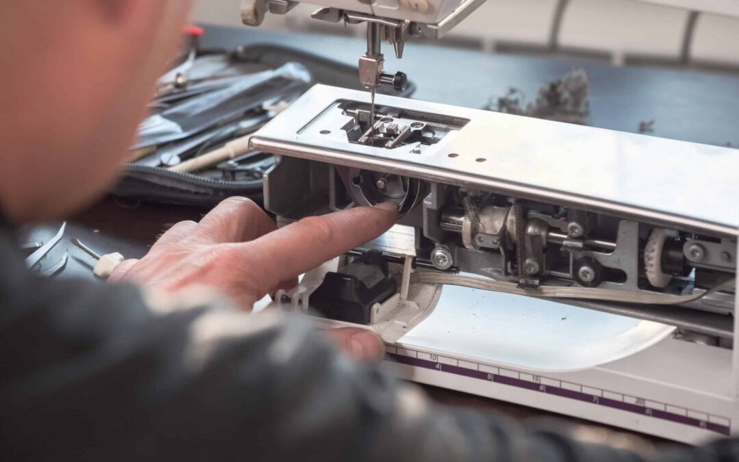 Male master repairs the sewing machine. Professional adjustment of a sewing machine in a small factory. Cleaning and repair of professional equipment.