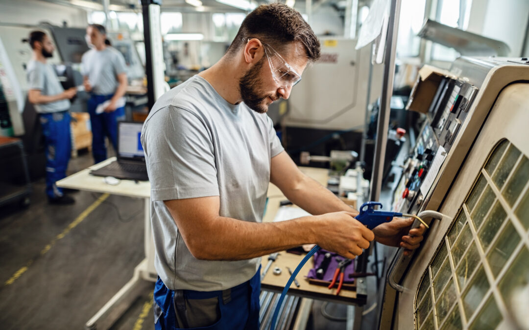 Young worker operating a CNC machine in industrial plant.